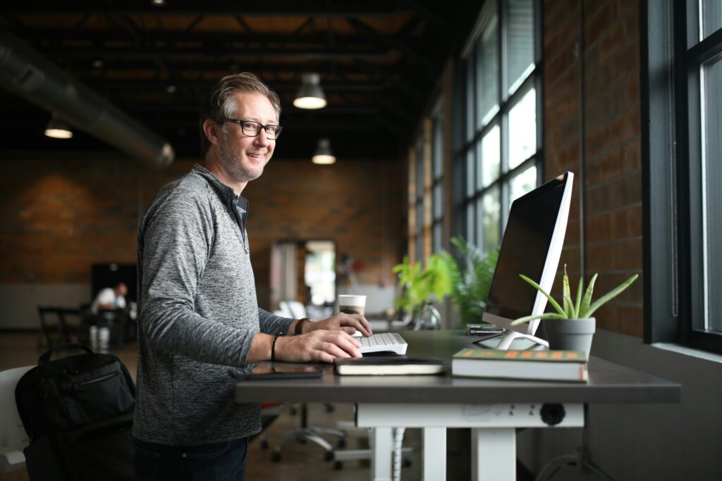 Man wearing glasses standing at height-adjustable desk using a computer and smiling