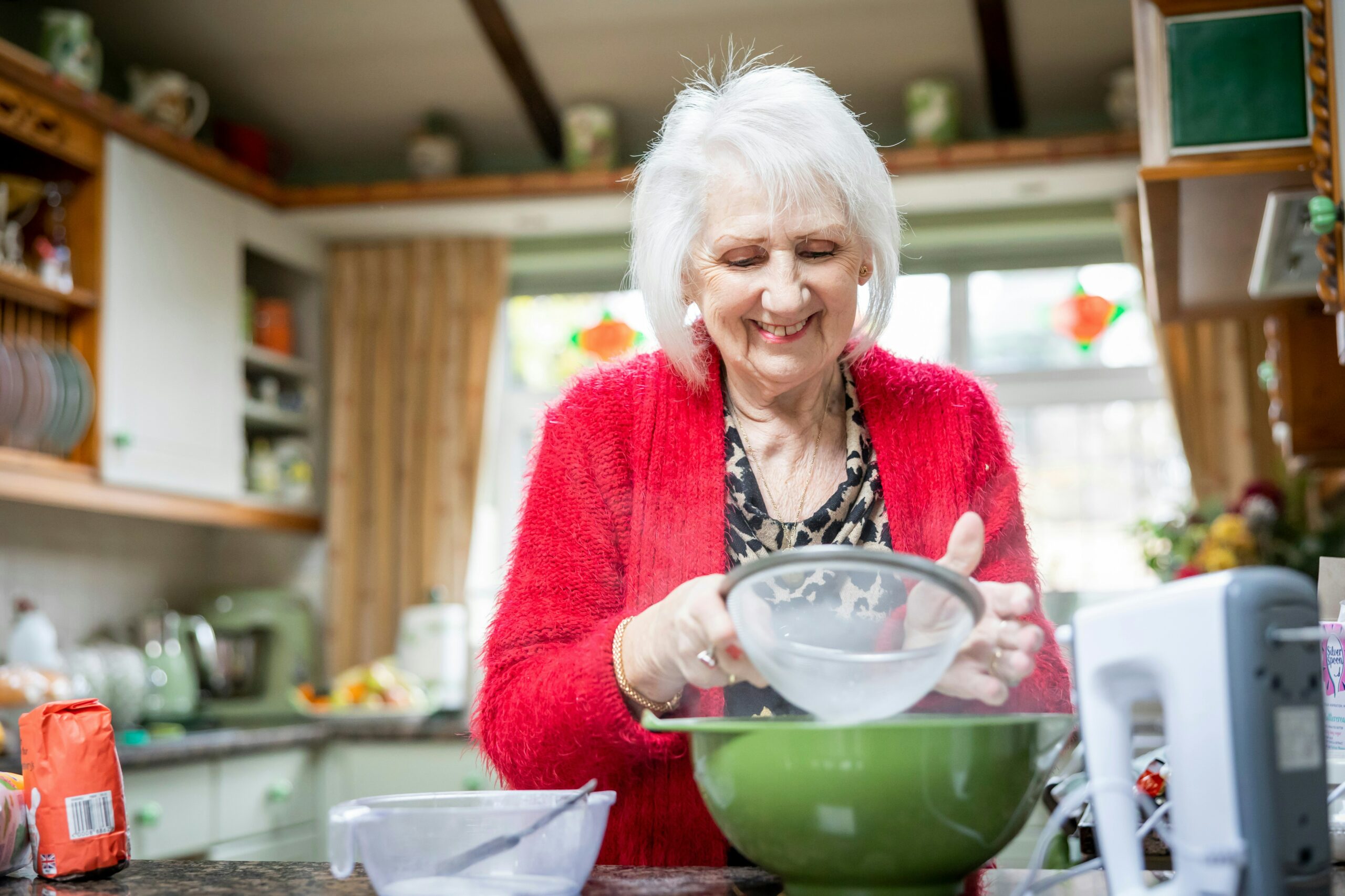 Smiling older woman using sifter over bowl placed on kitchen counter